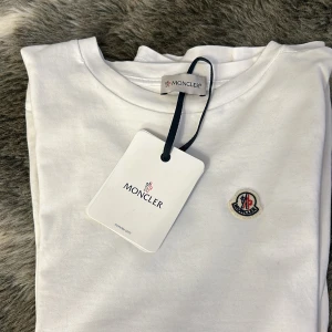 Moncler T-shirt vit  - Säljer en snygg vit t-shirt från Moncler i nytt skick. Den har en liten broderad Moncler-logga på bröstet och är kortärmad. Tags med kommer som sagt och den är använd 1-2 gånger. Passar längden 170-175cm och säljer eftersom den är för liten. Str 14Y men sitter som en XS.