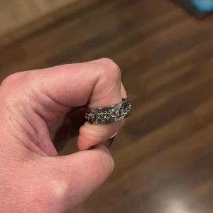 Silverfärgad ring med kedjedetalj - Snygg och stilren ring i silverfärg med en cool kedjedetalj runt om. Ringen är i storlek 8 och passar både till vardags och fest. Ringen är helt ny. 