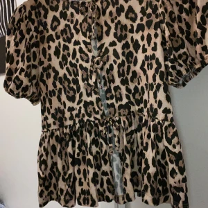 Leopardmönstrad blus - Säljer en superfin leopardmönstrad blus med korta ärmar och knyte framtill. Perfekt för en utekväll eller fest! Den har en lös passform och volangdetaljer vid midjan som ger en söt touch. Materialet känns mjukt och bekvämt. Skriv för fler bilder!✨🐆