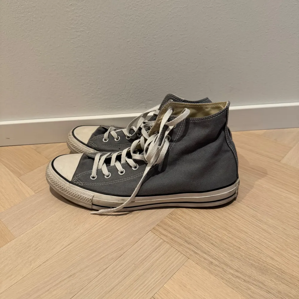 Säljer ett par klassiska grå Converse All Star sneakers i bra skick. De har vit snörning och den ikoniska loggan på sidan. Perfekta för vardagsbruk och passar till nästan allt. Sulan är i gott skick.. Skor.