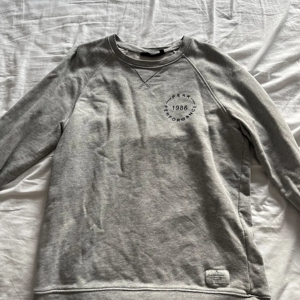 Säljer en stilren grå sweatshirt från Peak Performance. Tröjan har en rund hals och långa ärmar, perfekt för en avslappnad look. Den är i bra skick och har en liten logga på bröstet.. Neuletakit & Villapaidat.