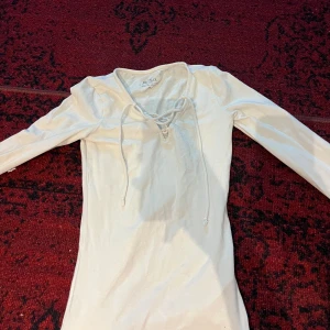 Vit långärmad topp från H&M - Säljer en stilren vit långärmad topp från H&M. Den har en snygg snörning framtill som ger en extra detalj. Perfekt för både vardag och fest! Passar bra till jeans eller kjol.