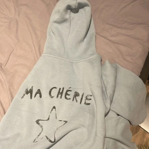 Grå hoodie från Gina Tricot - Säljer en supermysig grå hoodie från Gina Tricot med texten 'Ma Chérie' och en stjärna på framsidan. Perfekt för chilliga dagar eller när du vill vara bekväm men ändå snygg. Den har en klassisk huva och ribbade muddar. Passar perfekt till jeans eller leggings! Liten i storleken då de är storlek 166/152 säljer för 250