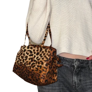 Leopardmönster väska - Liten väska i leopardmönster med rosetter på sidan. Sydd i tyg som är köpt secondhand! Mått: 16x27cm