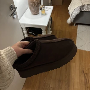 UGG - Säljer ett par bruna mockaskor. De är supermysiga och perfekta för höst och vinter. Skorna har en mjuk insida och en robust sula som ger bra grepp. Perfekta för att hålla fötterna varma och bekväma under kyliga dagar.