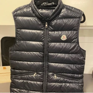  Moncler gui väst  - Säljer en snygg mörkblå Moncler gui väst i mycket bra skick. Västen är i storlek 3 men sitter som en xs.Västen är helt ny men kvitto,galge och extra knappar. Perfekt för höst och vår när du vill hålla dig varm men ändå se stilren ut.bara att skriva vid frågor samt intresse 👑👑