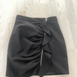 Svart kjol från Bik Bok - Snygg svart kjol från Bik Bok i storlek M. Kjolen har en cool dragkedjedetalj framtill och en stilren design. Perfekt för både vardag och fest! 🖤