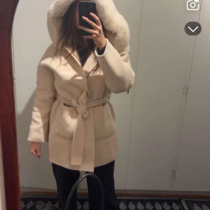 Beige kappa  Skåne  -  beige kappa med  huva . Kappan har ett knytbälte i midjan för en snygg passform och långa ärmar. Perfekt för kyliga dagar när du vill hålla stilen. Jackan har använts 3 gånger annars är den helt ny  