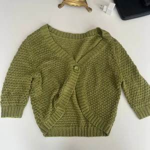 Olivgrön stickad kofta - Säljer en mysig olivgrön stickad kofta med en stor knapp framtill. Koftan har en fin struktur och trekvartsärmar, perfekt för lager på lager-stil. 💕