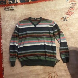 Randig tröja från U.S. Polo Assn. - Säljer en snygg randig tröja från U.S. Polo Assn. i olika färger som grön, blå, röd och vit. Tröjan har en v-ringad hals och långa ärmar, perfekt för en avslappnad stil.