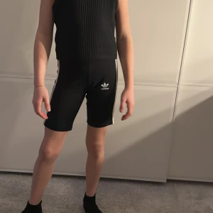 Svarta shorts från Adidas - Snygga svarta shorts från Adidas med de klassiska tre vita ränderna längs sidorna. Perfekta för träning eller en avslappnad dag. De har en tight passform och är tillverkade i ett bekvämt material.
