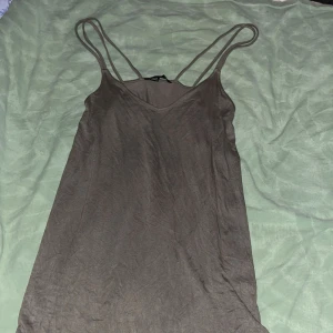 Brun/grön klänning med smala axelband - Säljer en enkel brun/grön klänning med smala axelband och v-ringning. Perfekt för en avslappnad stil. Tillverkad i ett mjukt och bekvämt material.
