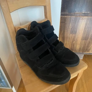 Svarta sneakers med kilklack - Snygga svarta sneakers med kilklack och kardborreband. Tillverkade i mocka för en mjuk och lyxig känsla. Storlek 38🥰