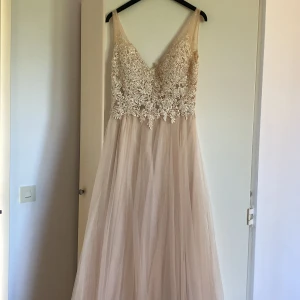 Champagnefärgad långklänning med spetsdetaljer - Elegant långklänning i champagnefärg med vacker spets upptill och en luftig kjol i tyll. Klänningen har en v-ringad urringning och är ärmlös. Använd 1 gång, tvättad och i fint skick. Nypris 2500kr