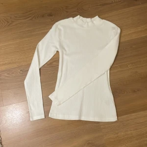 Vit ribbad långärmad topp - Säljer en stilren vit ribbad topp med långa ärmar. Perfekt för lager-på-lager eller som den är. Enkel och mångsidig design som passar till det mesta. Skön och stretchig för en bekväm passform.  Endast använd 1 gång!!