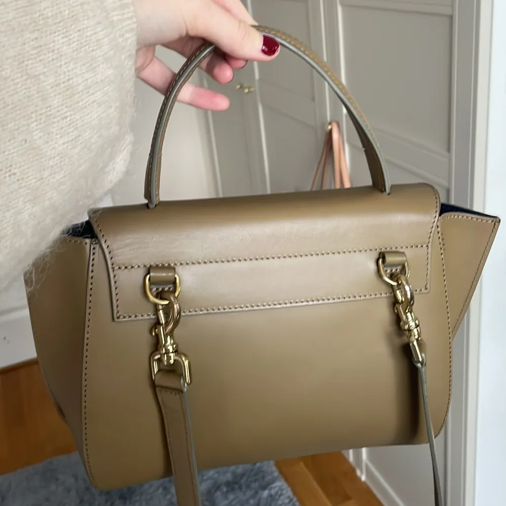 Snygg beige handväska i skinn med en unik asymmetrisk flikdesign. Väskan har ett handtag och en avtagbar axelrem för flexibilitet. Perfekt för att ge din outfit en stilren touch.. Laukut & Käsilaukut.