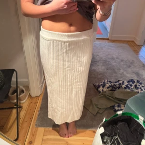 Vit ribbad kjol - Säljer en stilren vit ribbad kjol i lång modell. Kjolen har en elastisk midja för bekväm passform och är perfekt för både vardag och festliga tillfällen.