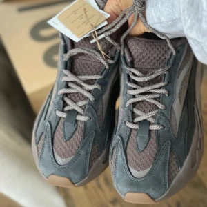 Adidas Yeezy Boost 700 V2 Mauve - Säljer ett par Adidas Yeezy Boost 700 V2 i en snygg kombination av grått och brunt. Skorna har en robust design med snörning och en bekväm sula. Perfekta för dig som vill ha både stil och komfort. Endast testade en gång inomhus. Passar dig som är en stl 39. 
