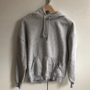 Grå hoodie  - Säljer en klassisk grå hoodie med justerbar dragsko i huvan och en stor magficka. Perfekt för en avslappnad stil och passar till det mesta. Skön och enkel att bära.