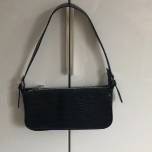 Svart axelväska med krokodilmönster - Snygg svart axelväska med krokodilmönster och dragkedja. Perfekt för att ge en stilren touch till din outfit. Enkel och elegant design.