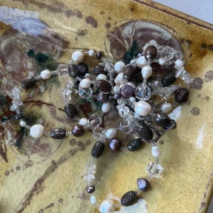 Långt halsband med pärlor och kristaller - Elegant långt halsband med en mix av vita och mörka pärlor samt klara kristaller. Perfekt för att ge en sofistikerad touch till din outfit. 