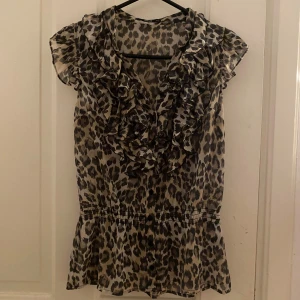 Leopardmönstrad blus - Snygg leopardmönstrad blus med volanger framtill och korta ärmar och resår i midjan 