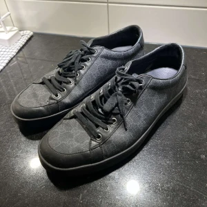 Svarta sneakers från Gucci - Svarta sneakers från Gucci med diskret mönster och snörning. Skorna har en stilren design och är super snygga och har en liten defekt 