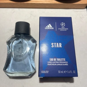 Adidas Champions League Star Eau de Toilette - Fräsch och långvarig doft från Adidas Champions League-serie. Flaskan har en unik form med en svart kork och rymmer 50 ml. Förpackningen är blå med en stjärndesign och Champions League-logotypen.