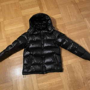 Moncler maya jacka - Snygg svart pufferjacka från Moncler med huva och dragkedja. Jackan har en glansig finish och är perfekt för kyliga dagar. Haft jackan i ett par månader, och den är i fint skick. Jackan är storlek 2, vilket motsvarar storlek M. Men den är liten i storleken så passar även S.