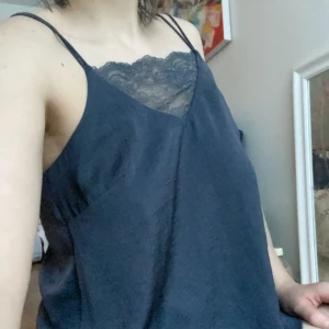 Mörkblå/grå linne med spetsdetalj - Snygg mörkblå linne från HM med spetsdetalj vid halsringningen. Perfekt för en stilren look med tunna axelband och en avslappnad passform. På vardera sida vid midjan har den en slits liknande form, syns på sista bilden 🥰