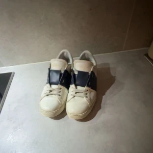 Beige sneakers med mörkblå detaljer - Snygga vita sneakers med mörkblå detaljer och snörning. Perfekta för en avslappnad stil. Skorna är väldigt bekväma för att vara designer skor. Skulle rekommendera att köpa dessa skor om du har storlek 39-40. De medföljer även en dusthbag.