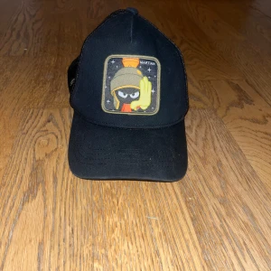 Svart keps från Capslab med Looney Tunes-motiv - Snygg svart keps från Capslab med ett broderat Looney Tunes-motiv på framsidan. Kepsen har en nätpanel baktill för bättre ventilation och en justerbar rem för perfekt passform. Perfekt för alla Looney Tunes-fans!