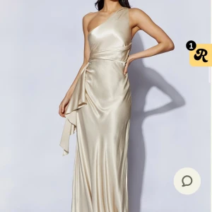 Balklänning - Elegant champagnefärgad långklänning i siden med en stilren oneshoulder-design. Den är från Meshki, andvänd en gång vid ett tillfälle. Klänningen har en vacker omlott-detalj i midjan som ger en smickrande passform. Perfekt för balen!💓💓💓(lång i längden)