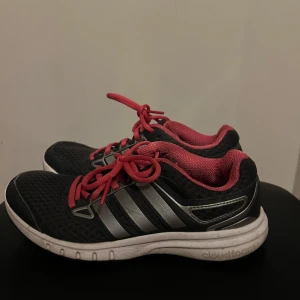 Svarta Adidas sneakers med rosa detaljer - Säljer ett par svarta Adidas sneakers med rosa snörning och insida. Skorna har de klassiska tre ränderna i silver på sidorna och en vit sula. Perfekta för träning eller vardagsbruk.