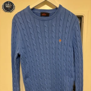  kabelstickad tröja från Morris - Säljer en snygg blå kabelstickad tröja från Morris i 100% Pima Cotton. Tröjan har en klassisk rund halsringning och ett diskret broderat emblem på bröstet.   Inga slitningar eller fläckar.                      👉 Just nu nytt plagg varje dag i 10 dagar – följ för att inte missa!