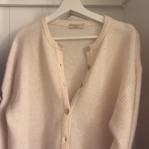 Beige kofta från Gina Tricot - Mysig beige kofta från Gina Tricot i premiumkvalitet. Den har en enkel design med knappar framtill och ribbade kanter. Perfekt för kyliga dagar.