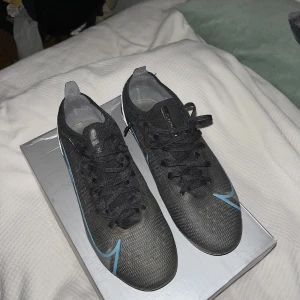 Svarta fotbollsskor från Nike | Vaper 14 Elite - Snygga svarta fotbollsskor från Nike med blå detaljer och snörning. Konstgräs dobbar (Ag). Använda 1 gång men var för små så därför jag säljer, inga skador eller slipor alls! Öppen för byte
