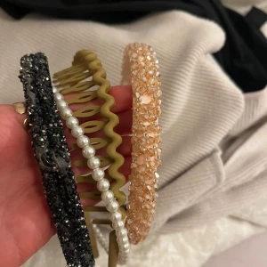 Flera stiliga diadem - Säljer ett set med fyra olika diadem. Ett svart glittrigt, ett med vita pärlor, ett beiget vågigt och ett beige/rosa med pärlor. Perfekt för att piffa upp vilken outfit som helst!