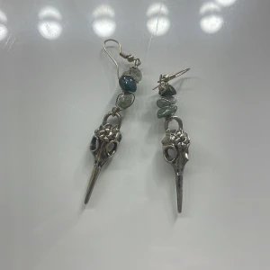 Unika örhängen med stenar och metallhängen - Säljer tre par unika örhängen, 130 kr per par och 79kr för sista. Första paret har silverfärgade fågelkranier med gröna stenar. Andra paret har handformade hängen med lila stenar. Tredje paret har en klar kristall i metalltråd. Perfekta för att ge en personlig touch till din stil. Dessa kommer inte till användning däför så säljer jag dem, de är i jätte bra skick!💕