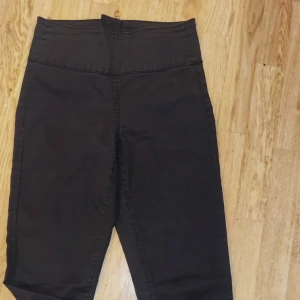 Svarta byxor med hög midja - Snygga svarta byxor med hög midja och dragkedja bak. Perfekta för en stilren look. Byxorna har en tight passform och är tillverkade i ett stretchigt material för extra komfort.