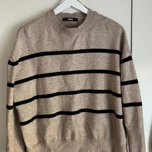 Stickad tröja - Brun och svart randig stickad tröja från bikbok, använd varsamt och i gott skick. Varken nopprig eller sliten. Säljer då den inte kommer till användning🤎