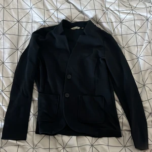 Svart kavaj från Tom Tailor - Säljer en stilren svart kavaj från Tom Tailor. Den har en klassisk design med två knappar framtill och två fickor. Perfekt för både vardag och festliga tillfällen. Passar bra till höst och vår.