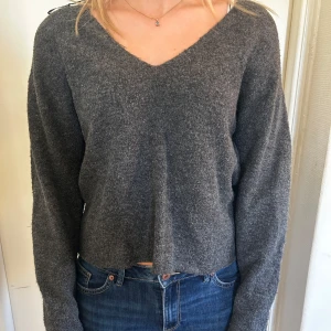 Grå stickad tröja med v-ringning - Säljer en supermysig grå stickad tröja med v-ringning. Den är perfekt för kyliga dagar och har en avslappnad passform. Tröjan är croppad och har långa ärmar, vilket gör den både stilren och bekväm.