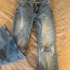 Blå jeans med slitningar - Säljer ett par snygga blå jeans från Gina tricot i storlek 36. De har en slitning på ena knäet och botcat.