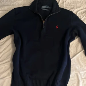 Mörkblå tröja från Polo Ralph Lauren - Säljer en snygg mörkblå tröja från Polo Ralph Lauren i storlek M. Tröjan är gjord av 100% bomull och har en dragkedja vid halsen. Den har en klassisk design med det ikoniska röda Polo-logotypen broderad på bröstet. Perfekt för höst och vinter!