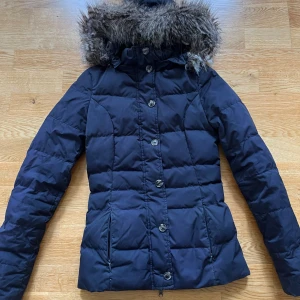 Tommy hilfiger dunjacka - Säljer en marinblå Tommy hilfiger dunjacka med knappar och dragkedja som stängning. Antagbar luva samt päls. I bra skick! Storlek xxs