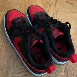 Svarta och röda Nike sneakers - Säljer ett par snygga Nike sneakers i svart och rött. De har en klassisk design med röd Nike-logga på sidan och svart ovandel. Skorna har en vit sula och är perfekta för både vardag och träning. De är i bra skick och redo för en ny ägare!