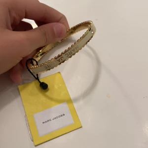 Guldarmband från Marc Jacobs - Säljer ett snyggt guldarmband från Marc Jacobs. Armbandet har en elegant design med en fin detalj av en liten sten. Perfekt för att ge en touch av lyx till vilken outfit som helst. Kommer med originaletikett. Värd 1299kr 