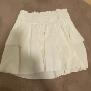 Vit volang kjol  - En mycket fin vit kjol med subtila volanger. Har inget ”skydd” innuti. Kjolen är i storlek petite M men kan passa en större S