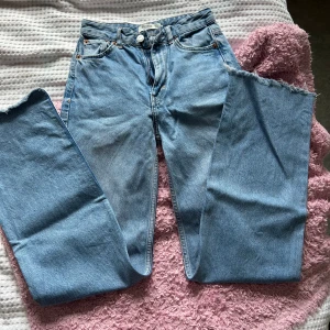 Blå jeans med fransiga kanter - Säljer ett par snygga högmidjade blåa jeans med fransiga kanter. De har en klassisk femficksdesign och en knappgylf. Perfekta för en avslappnad stil! 